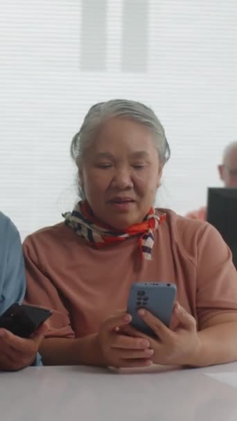 坐在同学旁边 一边带着智能手机一边上电脑课 一边兴高采烈的亚裔妇女的垂直肖像 — 图库视频影像