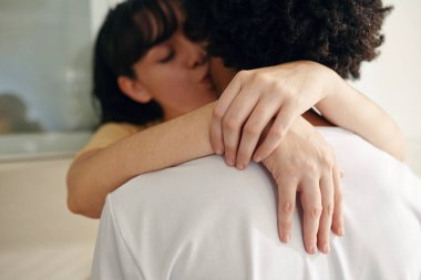 Gözleri kapalı genç bir kadının elleri kocasını boynundan kucaklıyor ve kameranın önünde onu öpüyor.