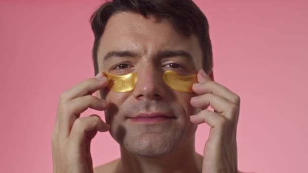 ピンクの背景のカメラで笑顔の黄色い目のパッチを持つ陽気な中年の男性のスタジオショット — ストック動画