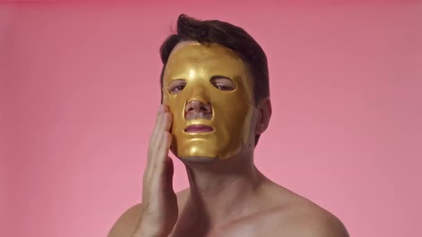 头像演播室拍摄的短发男子 棕色眼睛 头戴金色水化薄片面具 脸隔离在粉红色中 — 图库视频影像