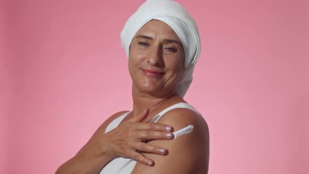 演播室里拍摄的快乐的成熟女人穿着毛巾纸 手臂上涂着水合作用的护肤霜 看着相机 — 图库视频影像