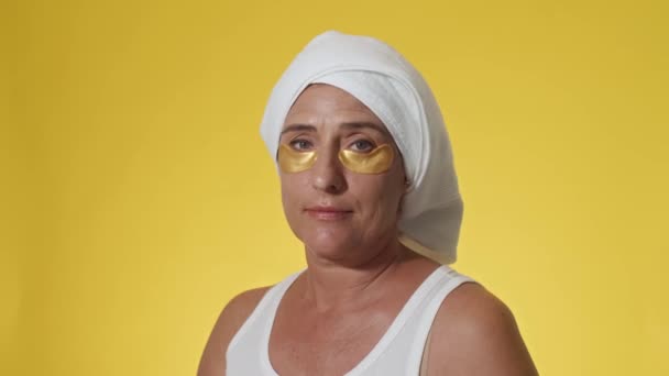 中老年白种人妇女头戴发巾 头戴白色上衣 眼皮底下贴着黄底相机微笑的肖像照 — 图库视频影像