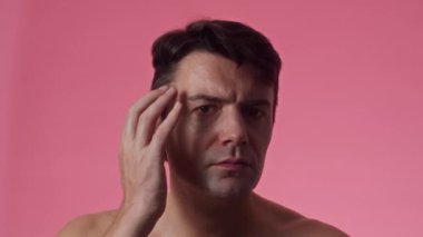 Neşeli Y 'li adamın saçını düzeltirken ve pembe arka planda kameraya gülümserken çekilen portre resmi.
