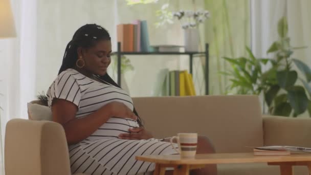 非洲裔美国孕妇坐在沙发上咖啡桌上 对着相机微笑 — 图库视频影像