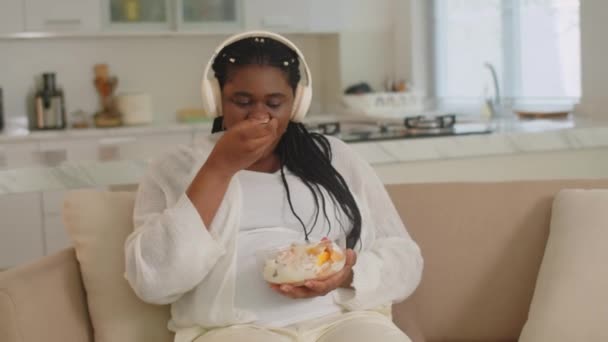 Середній Знімок Щасливої Вагітної Африканки Їсть Фруктовий Салат Слухає Музику — стокове відео