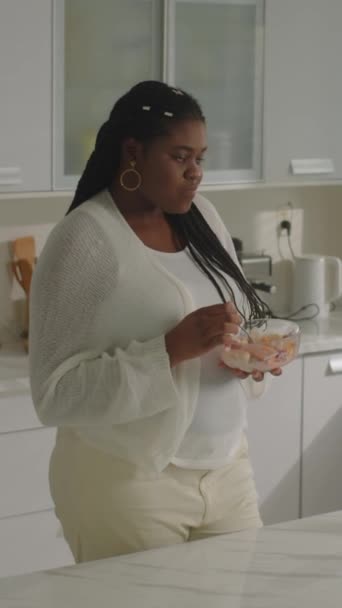 Pionowe Ujęcie Czarnej Kobiety Ciąży Jedzącej Śniadanie Głaskającej Brzuch Kuchni — Wideo stockowe