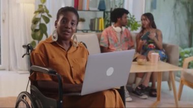 Özürlü neşeli bir kadının portresi dizüstü bilgisayarda çalışıyor arka planda arkadaşları var, kameraya bakıyor.