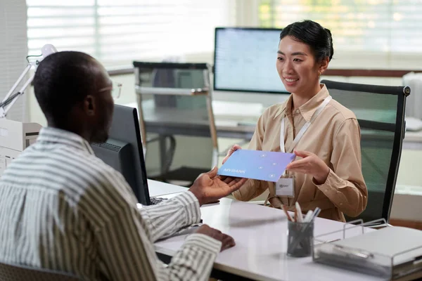 Smiling bank manager giving client envelope with offers