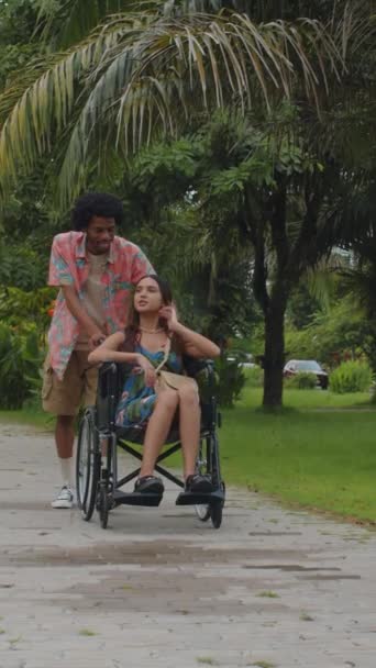 Afro Amerikan Bir Adamın Asyalı Kız Arkadaşının Tekerlekli Sandalyesini Iterken — Stok video