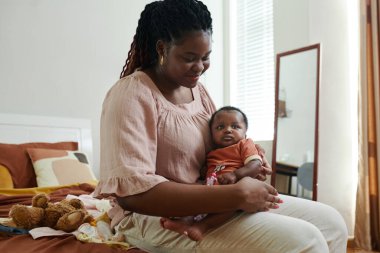 Gülümseyen siyah kadın kucağında küçük kızıyla yatakta oturuyor.