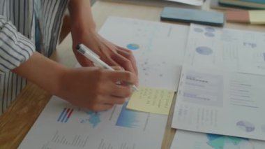 Yapıştırmaya yazı yazan kadın analistin ellerini kapatırken masadaki kağıt üzerinde iş istatistikleri derleniyor
