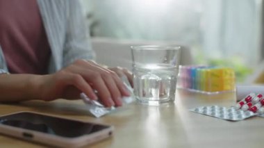 Tanımlanamayan bir kadının sıcak tableti evdeki masada suyla dolu bir bardağa koyarkenki görüntüsü.