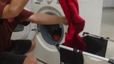 Delikanlının evde temizlik yaparken çamaşır makinesine koyu renk çamaşır koyması.