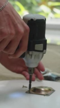 Masayı evde monte ederken tanınmayan bir adamın metal matkapla deldiği dikey çekim.