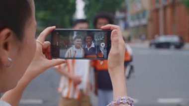 Şehirdeki erkek arkadaşlarının fotoğraflarını çekerken akıllı telefonu gözünün önünde tutan kadının omzunun üstünden.