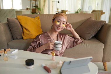 Smiling woman enjoying selfcare day, drinking tea, watching movie after taking bath clipart