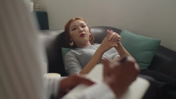 若いアジアの女性は 心理学者とのセッション中にソファーに横たわっている間に彼女の症状を説明します — ストック動画