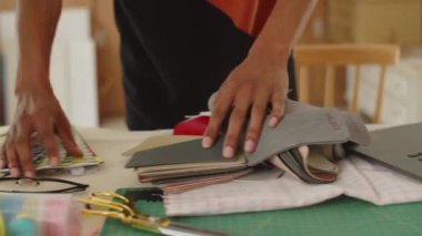 Kumaş örnekleriyle çalışan ve dizüstü bilgisayardaki bilgileri kontrol eden tanınmayan bir denizcinin el görüntüsü.