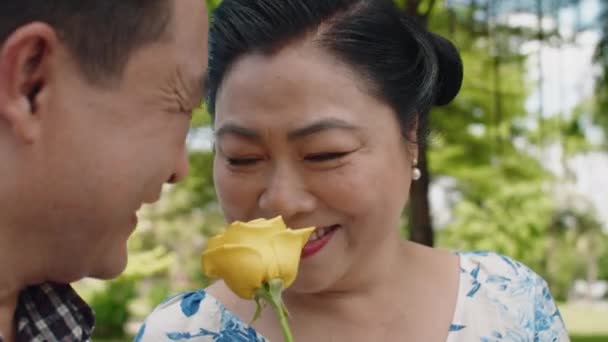 成熟したアジアの女性のクローズアップは 彼女に与えられた黄色の花に喜び 屋外で夫を愛するからプレゼント — ストック動画