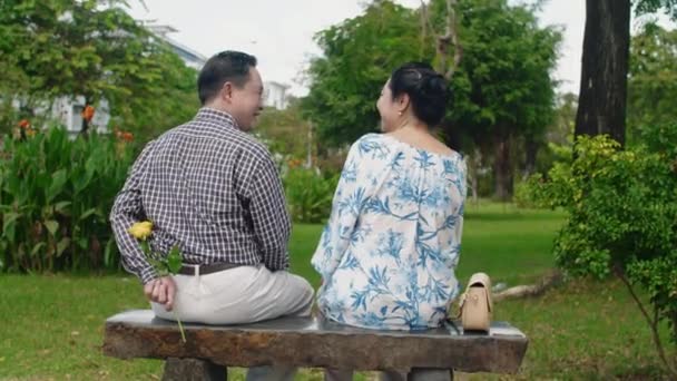 バラの後ろに隠れてベンチに座っている夫の背中を見ると 公園で散歩中に妻に与える — ストック動画