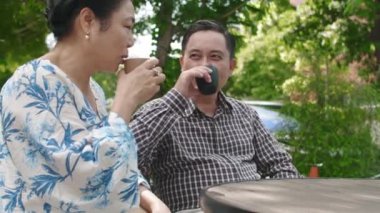 Yetişkin bir eşin yaz bahçesinde birlikte çay içerken kocasıyla konuşmasının yan görüntüsü.