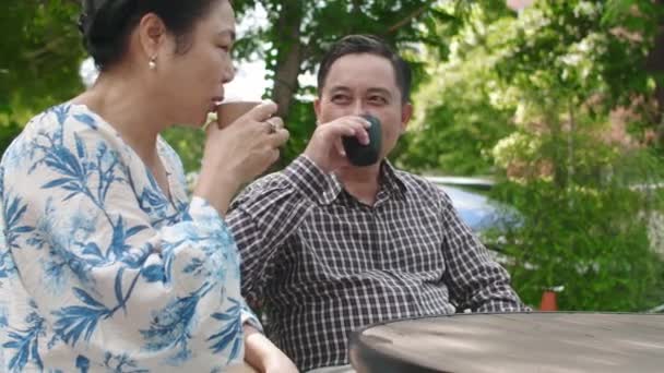 成熟した妻のサイドビュー 夫と話しながら一緒にテーブルに座って紅茶を飲む 夏の庭 — ストック動画