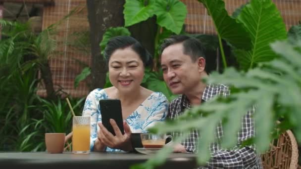 카페에서 테이블에 스마트 자신의 손자의 사진을보고 즐거운 성숙한 아시아 배우자의 — 비디오