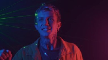 Genç adamın gece kulüpte neon ışıkta dans ederken orta boy fotoğrafı.