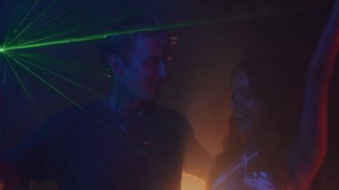Farklı çiftlerin loş bir gece kulübünde flört edip dans etmelerinin yan görüntüsü.