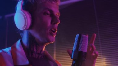 Genç beyaz erkek şarkıcının gece kulübünde neon ışıklı mikrofonda şarkı söylemesini kapatın.
