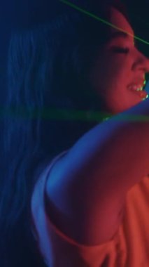 Neon partisinde gece kulübünde tek başına dans eden neşeli genç bir kadının dikey çekimi.