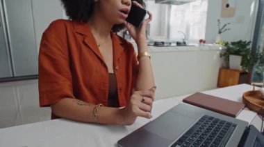 İspanyol iş kadınının cep telefonuyla konuşurken görüntüsünü kaldır ve evdeki laptoptan bilgileri kontrol et.