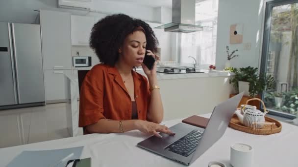 自宅でワイヤレスラップトップでレポートしながら同僚に電話する女性マネージャーの広いショット — ストック動画