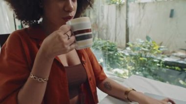 Evde bilgisayardaki iş çizelgelerini incelerken genç bir kadının kahve içerken görüntüsünü öne eğ.