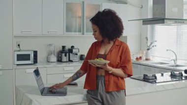 Latin kadının evde salata yerken laptoptan haber okuduğu geniş açı.