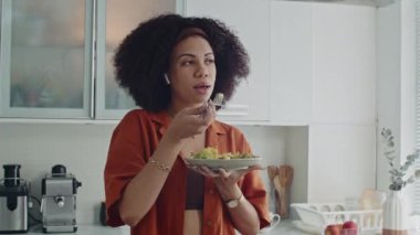 Latin kadının salata yerken kulaklık taktığı ve arkadaşlarıyla konuştuğu orta boy bir fotoğraf.