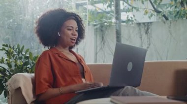 Rahat kadın finans danışmanının yan görüntüsü dizüstü bilgisayarın önünde otururken evden müşteri arıyor.