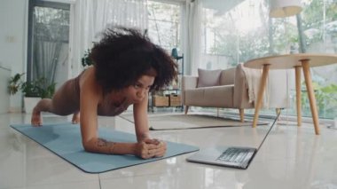 Genç İspanyol sporcunun evdeki dizüstü bilgisayarında online fitness uygulaması kullanarak tahta egzersizi yaptığı uzun bir çekim.