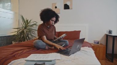Kıvırcık kadın girişimcinin online toplantıya hazırlanıp laptopun önünde yatakta oturması.