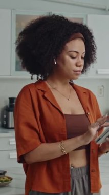 Evde dijital tablet üzerinde çalışırken kameraya poz veren genç iş kadınının dikey portresi