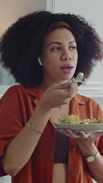 中午在家吃沙拉的时候 带着耳机和朋友聊天的拉美裔女人的垂直照片 — 图库视频影像