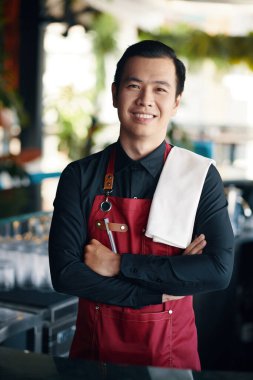 Sırıtan Vietnamlı barmen omuzlarında havluyla restoranda çalışıyor.