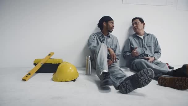 Pan Tiro Dois Trabalhadores Construção Diversos Sentados Chão Durante Intervalo — Vídeo de Stock