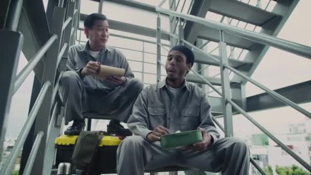 階段で休憩しながら 灰色の制服でフォアマンとビルダーのローアングルショット — ストック動画