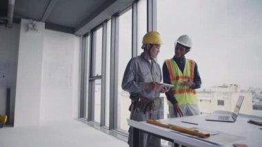 İki melez inşaat işçisinin tablet bilgisayardaki planlara bakarken gün boyu çalışmayı planlarken geniş açı