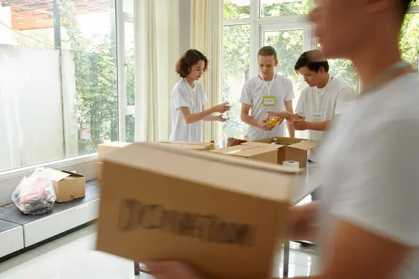 慈善団体でボランティア活動する若者の多様なグループ 箱に食糧を詰め込む ロイヤリティフリーのストック画像