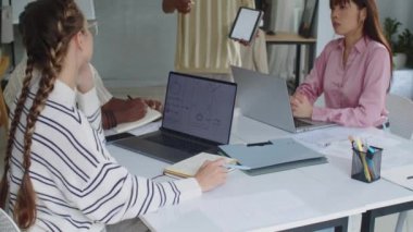 Tablet bilgisayarında uygulama arayüzü gösteren ürün yöneticisini dinleyen genç geliştiricilerin görüntüsünü yukarı kaldır