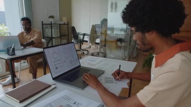 坐在笔记本电脑前的从事移动应用程序接口工作的黑人男性Ux设计者的侧视图 — 图库视频影像