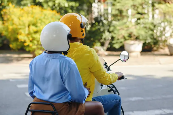Motorbike taxi driver and passenger in helmets riding in city, view from the back
