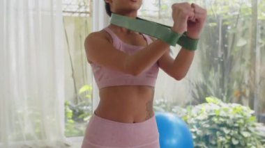 Asyalı sporcunun içeride çalışırken direnç eğrisiyle egzersiz yaparken çekimini yukarı kaldır.